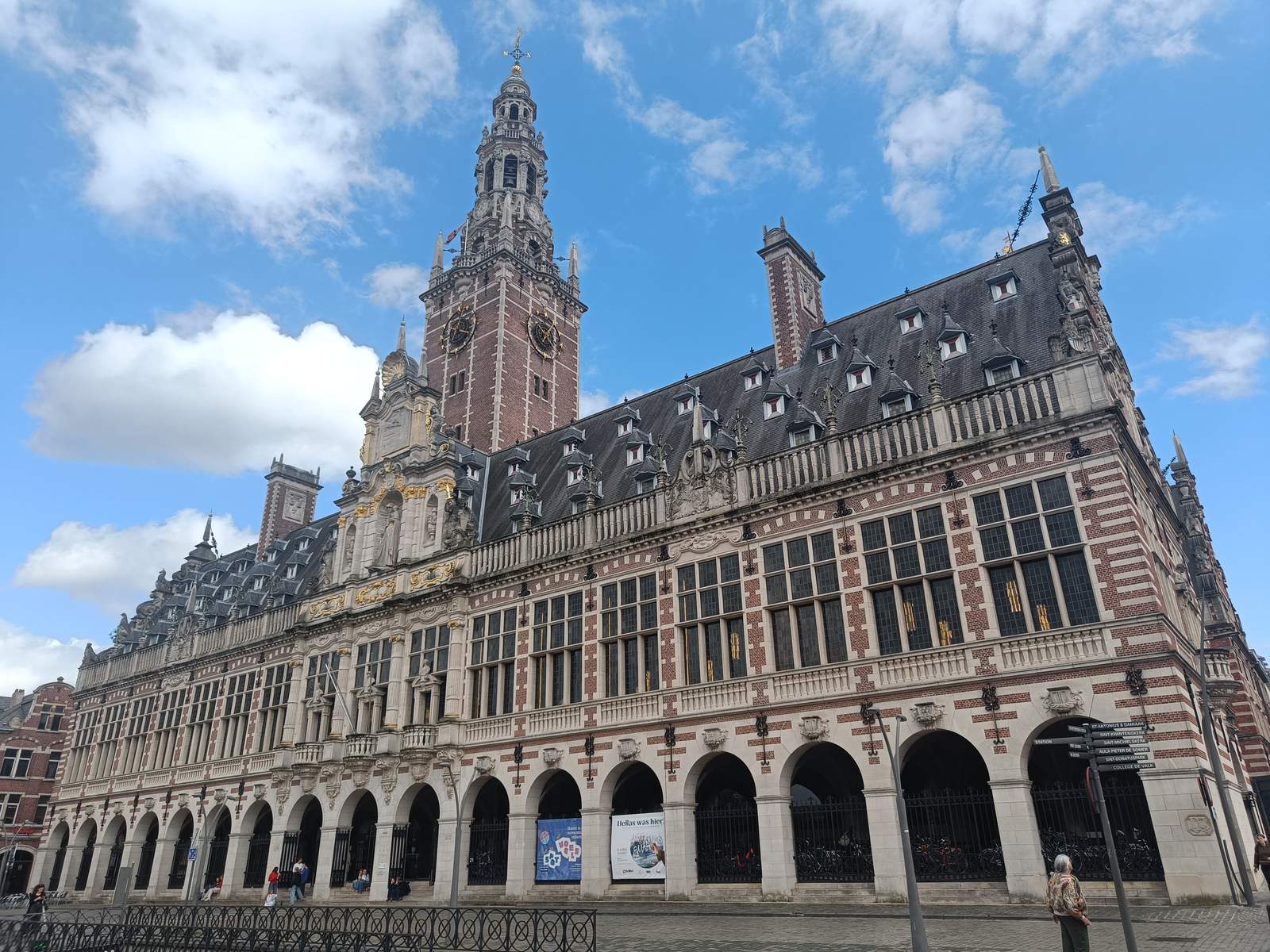 The Flemish Renaissance-style University Library of KU Leuven, with its tall ornate bell tower, arcaded ground floor and red-and-white brickwork under a blue sky